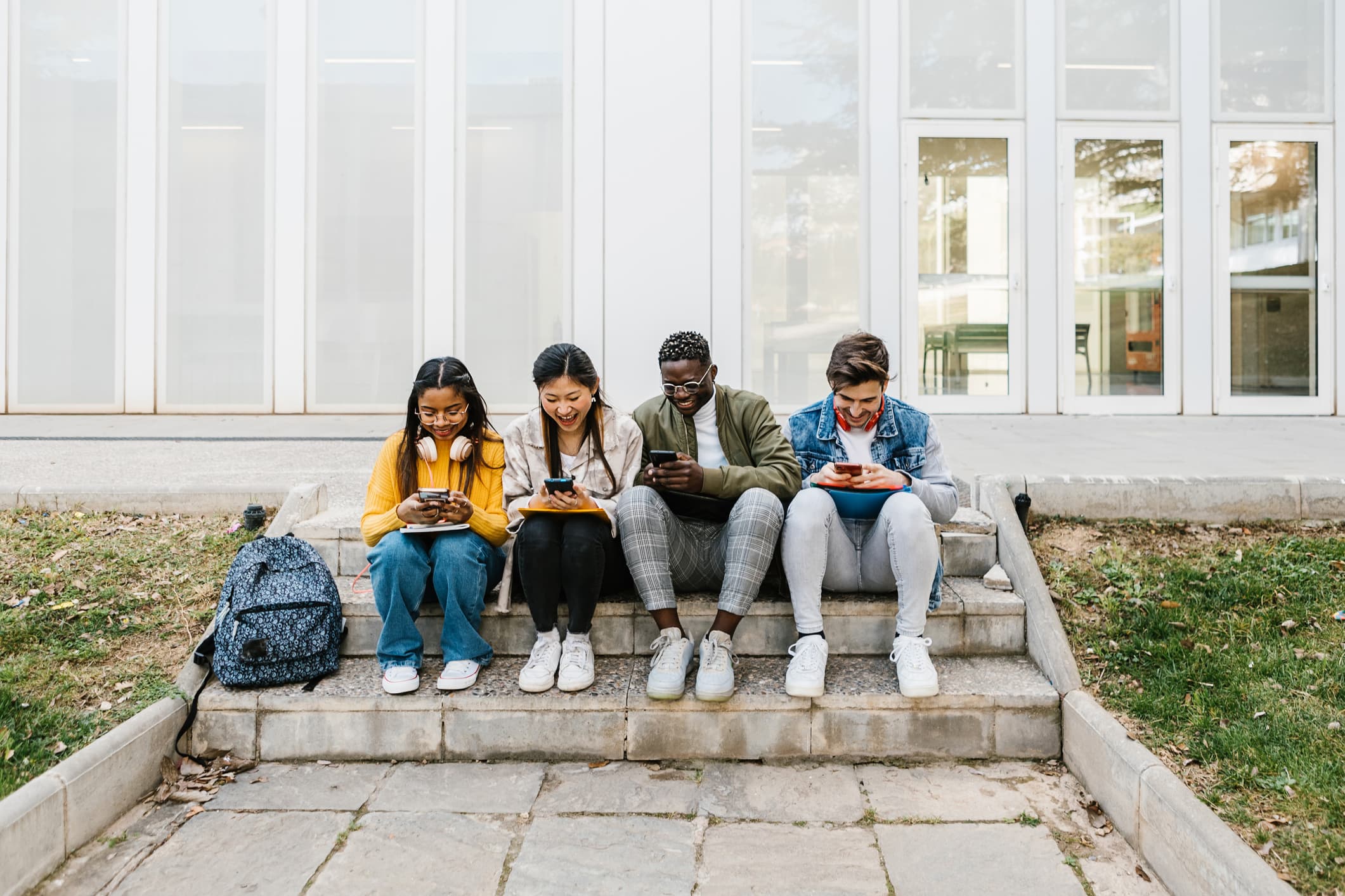 Young multiracial students using cell phone sitting at campus school