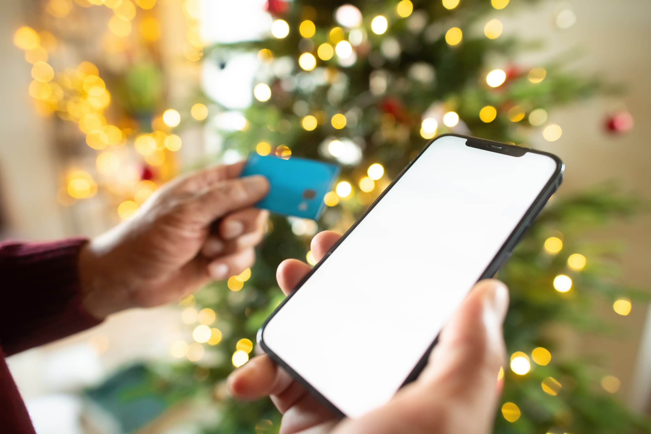 Man with smartphone and credit card near Christmas tree